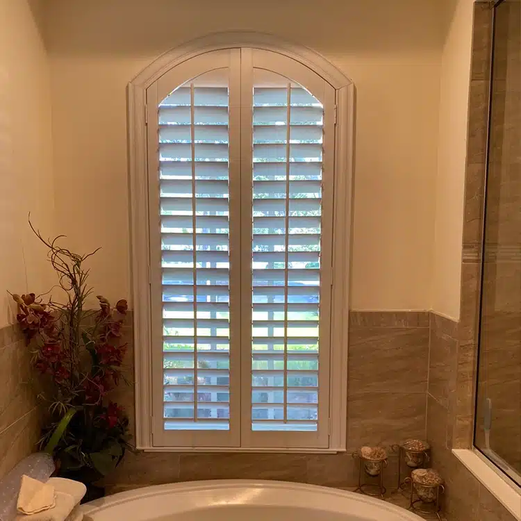 Window beside a bathtub with custom plantation shutters closed for privacy