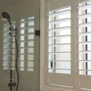 Shower with custom solid composite shutters over the window for privacy and sunlight control